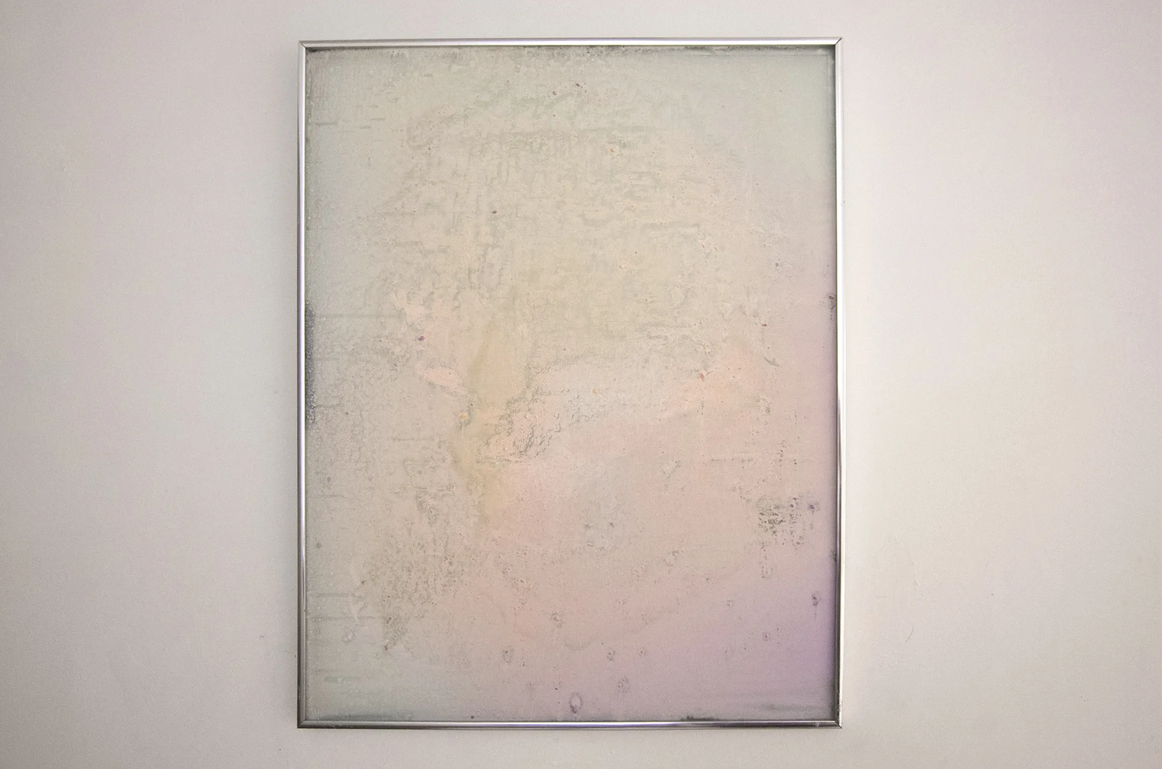 Fool-A-Roo, installation view A silver-framed panel of pale iridescent residue in mother-of-pearl pinks and greens, hung on a white wall.
